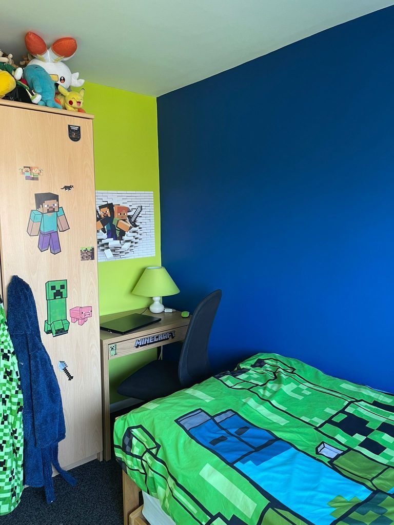 A child’s bedroom with a dark blue wall, a lime green wall, a Minecraft-themed bed, a desk, and a wooden wardrobe.