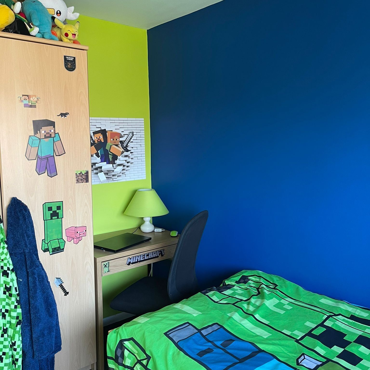 A child's bedroom featuring Minecraft-themed decor, including a green creeper bedspread, stickers, and blue and lime walls.