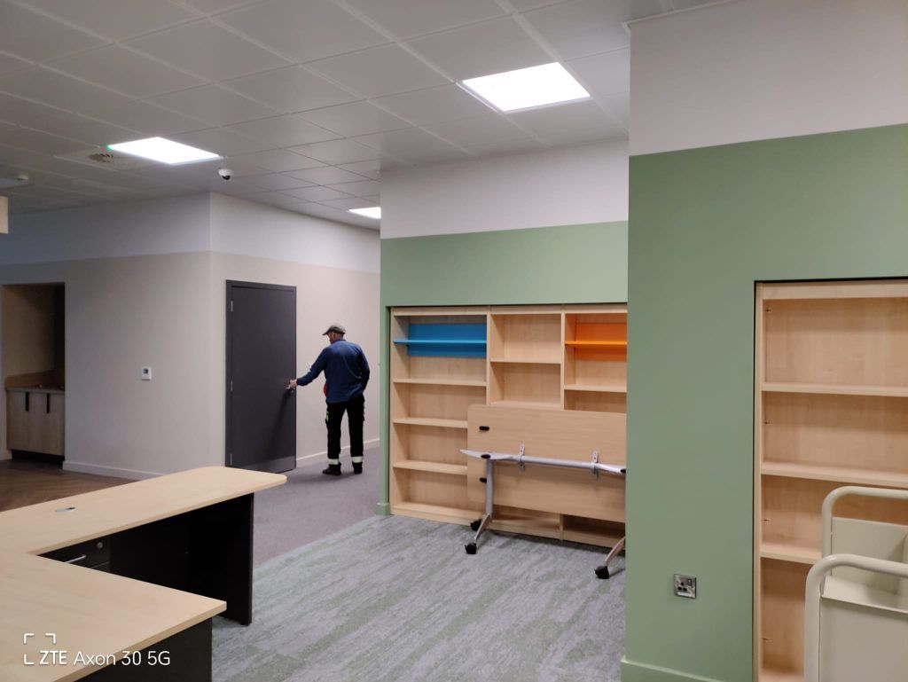 A person in a blue shirt opening a dark door in a modern office space with light-colored shelving units and green accents.