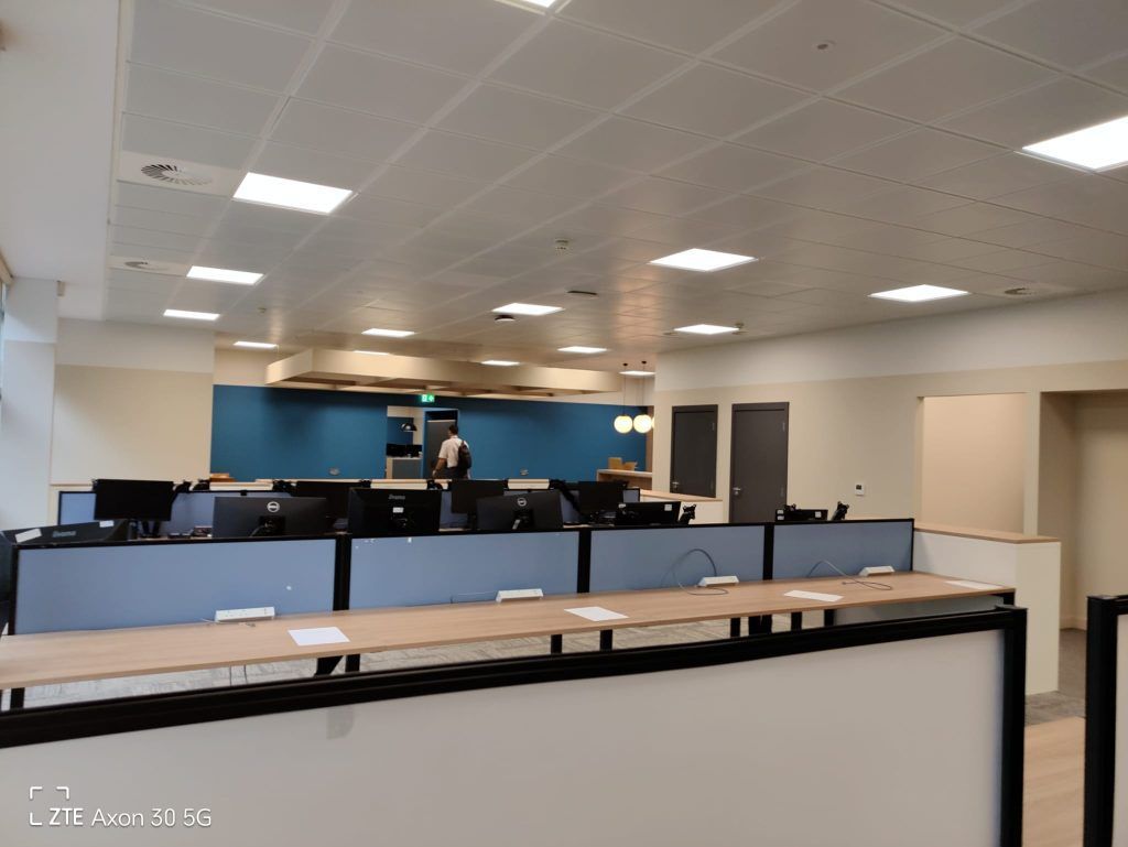 An office space featuring rows of workstations with light wood desks, blue privacy screens, and computers.