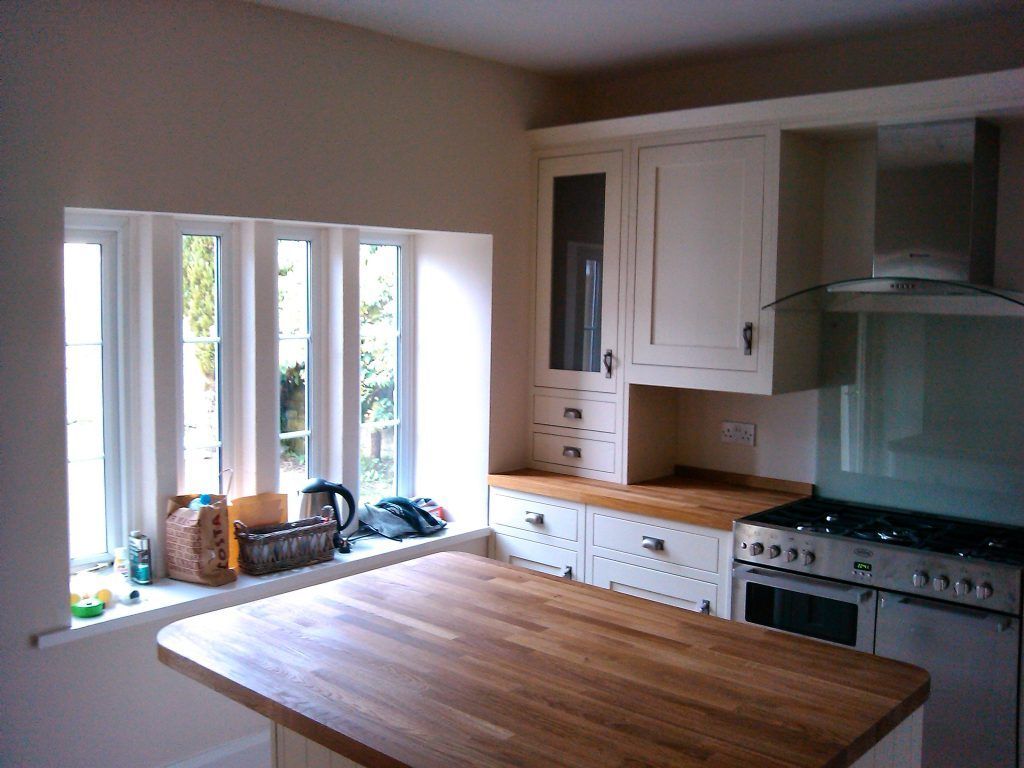 Kitchen with a wooden island, white cabinets, a stainless steel stove, and a window with a view of greenery.