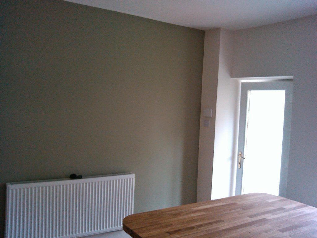 A room with a beige wall, a white radiator, and a glass-paneled door, partially obstructed by a wooden tabletop.