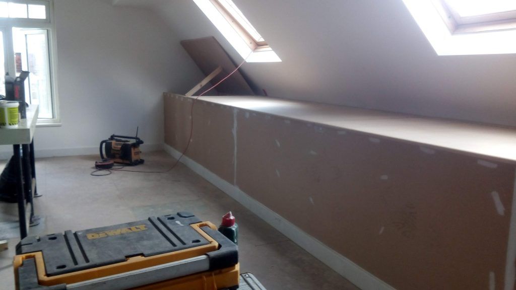 A room undergoing construction, featuring newly installed drywall along a slanted attic wall and a toolbox in the foreground.