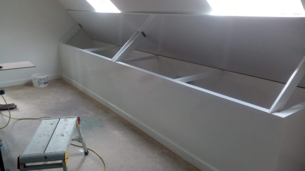 White finished knee-wall storage built-ins with angled tops under attic skylights, with a step stool nearby.