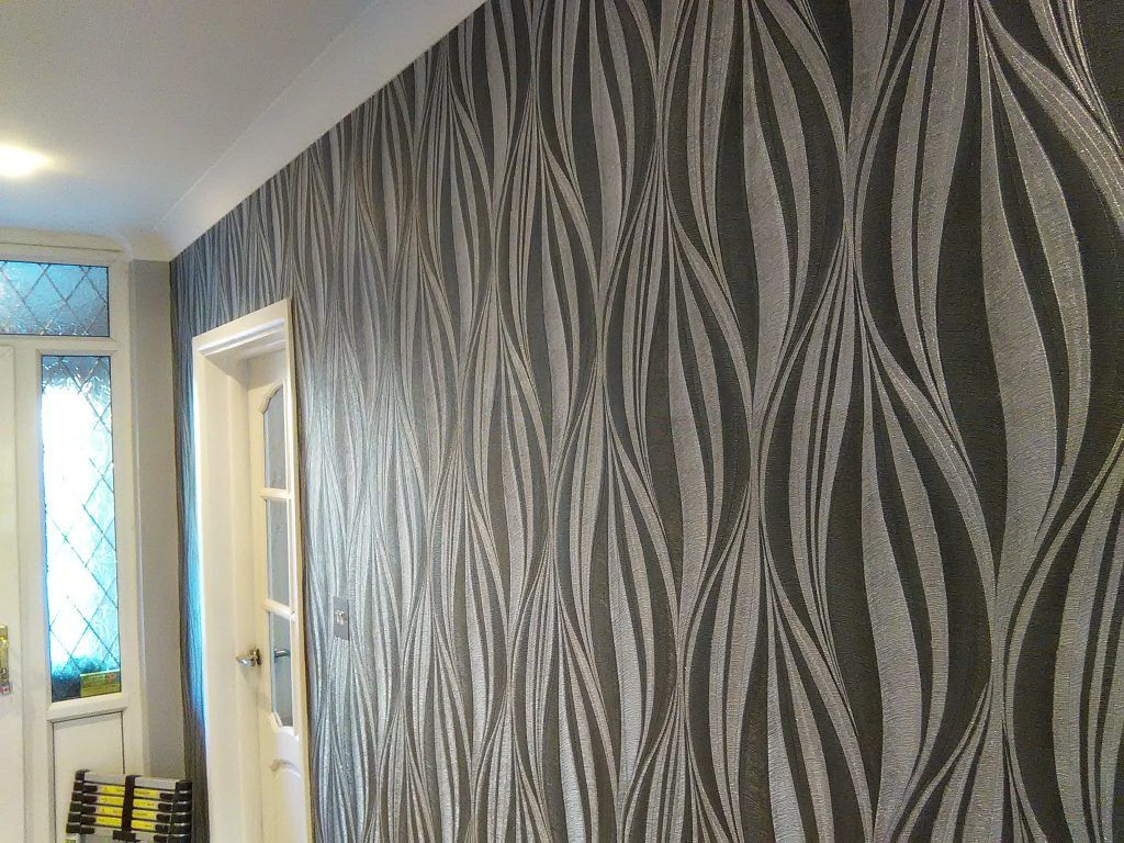An interior view showing a wall covered in dark wallpaper with a repeating, vertical silver leaf pattern, next to a door.