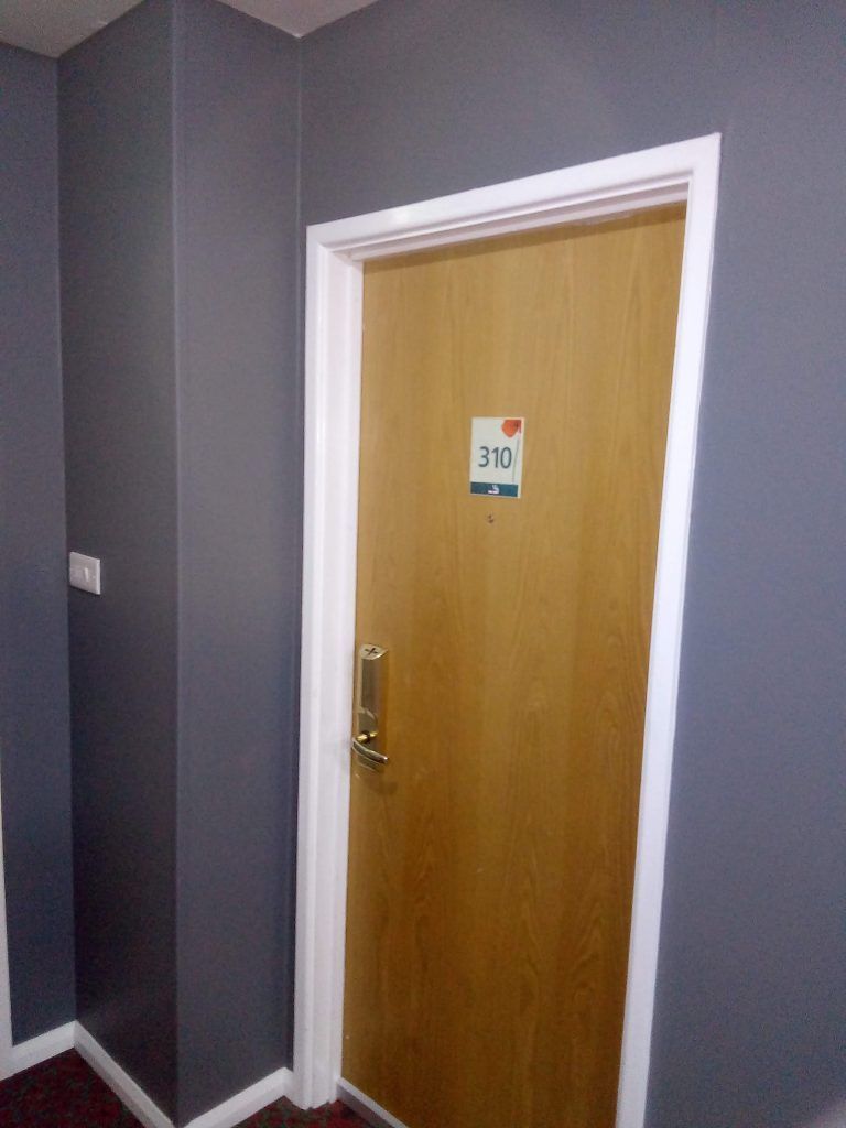 A light wood hotel room door numbered 311, set against a dark gray wall with white trim and a silver handle.