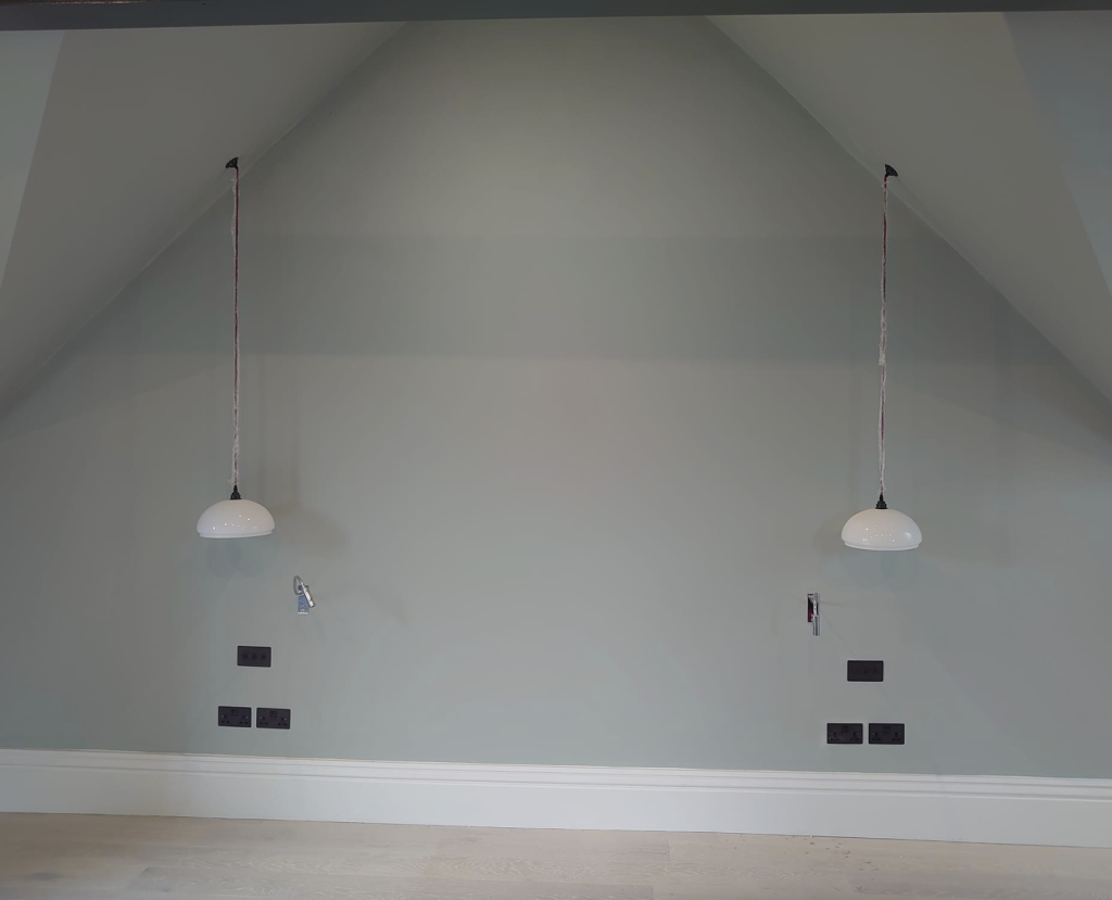 A gray bedroom wall with a peaked ceiling, two white pendant lights, and electrical outlets for bedside tables.