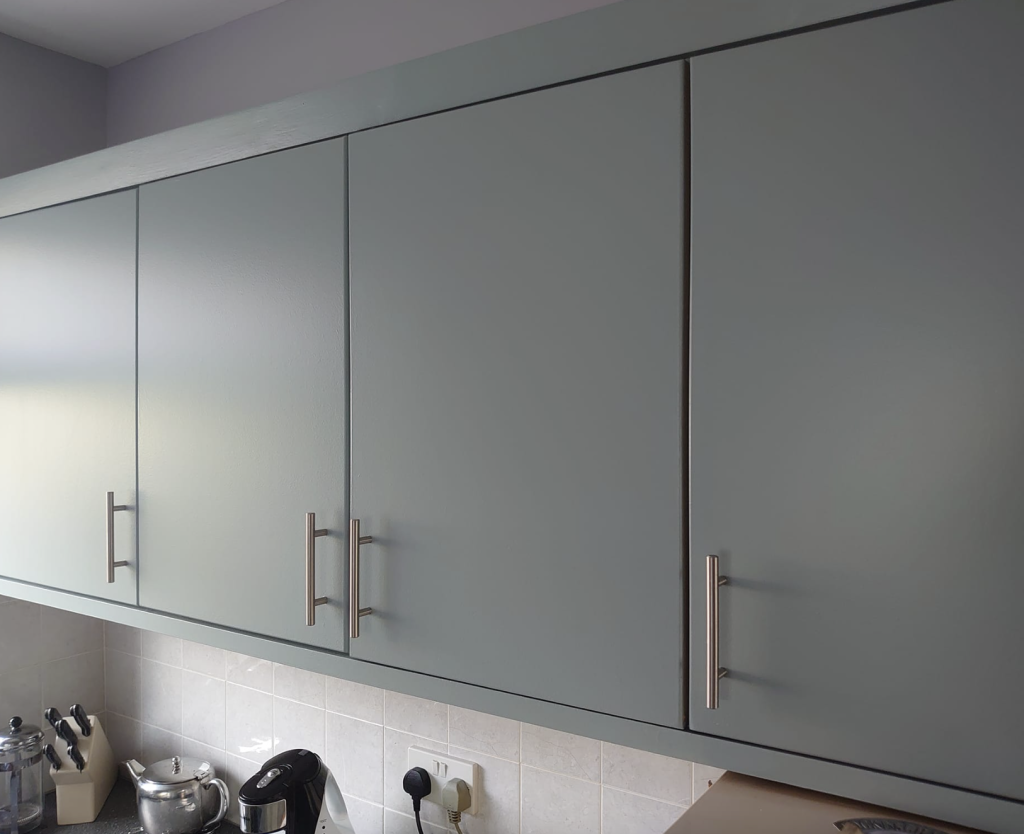 Gray kitchen cabinets with silver T-bar handles installed above a white tiled backsplash and kitchen appliances.