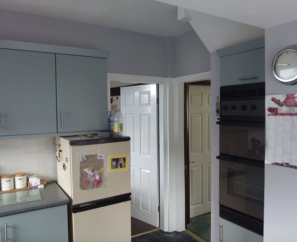 A kitchen featuring grey cabinets, a cream refrigerator with notes, a wall-mounted oven, and open doorways to other rooms.