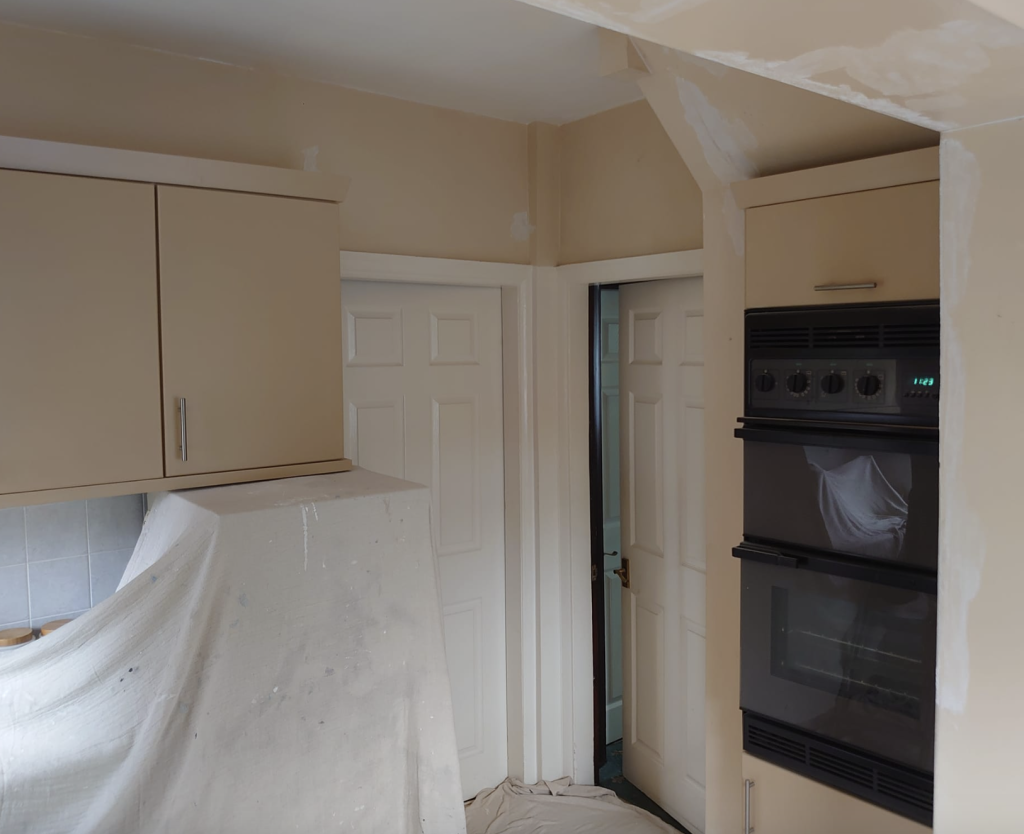 A kitchen under renovation featuring beige cabinets, a built-in double oven, and walls partially covered in white filler.