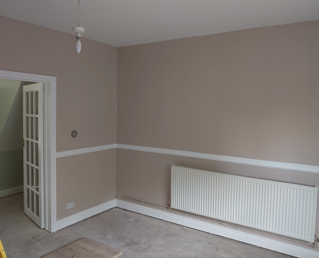 A room with taupe walls, white trim, a chair rail, and a horizontal white radiator under a white-paned door.