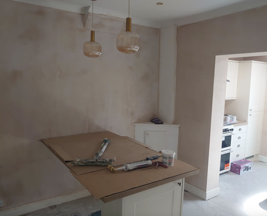 A renovated room with fresh plaster walls, pendant lights, a covered kitchen island, and a doorway to a kitchen area.