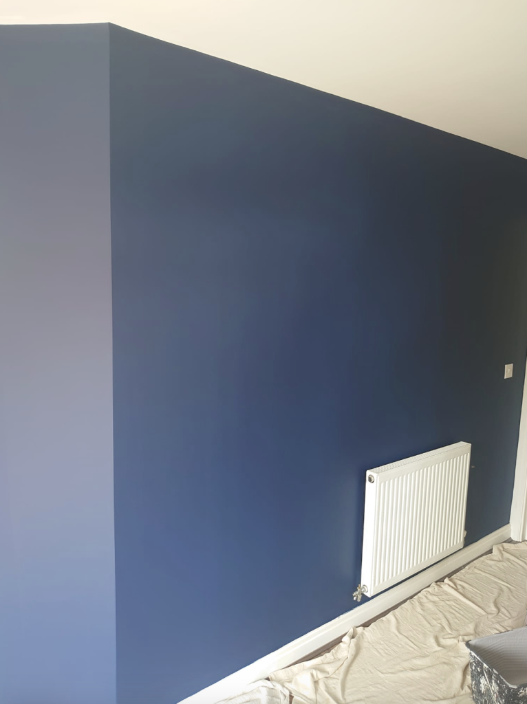A room interior featuring a freshly painted navy blue wall with a white radiator, against a protective floor drop cloth.