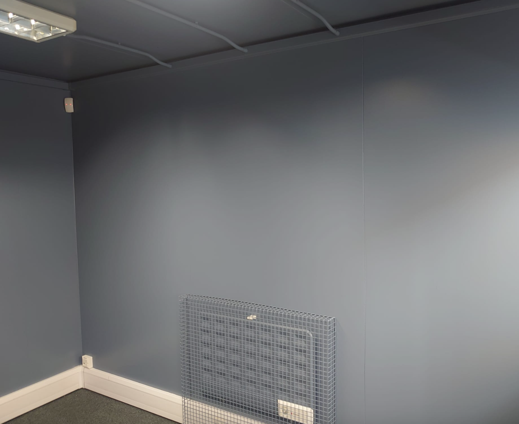 A corner of a room with blue-gray walls, a white baseboard, a ceiling light, and a wire grate leaning against the wall.