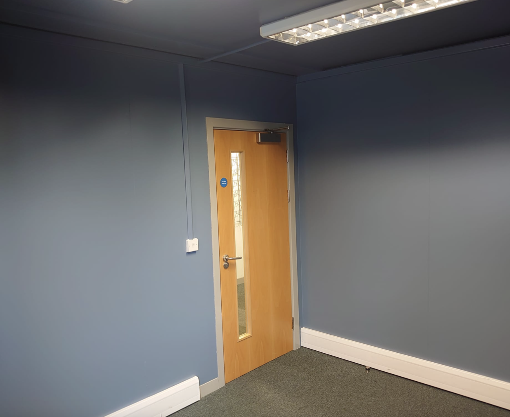 An interior corner with blue walls, carpet, and a wooden door featuring a glass panel and metal push plate.