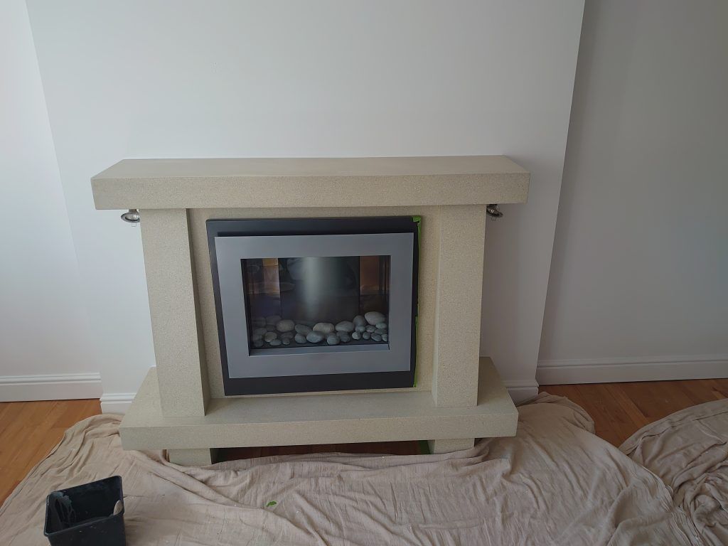 A light-colored stone fireplace mantle surrounding an electric insert with faux rocks, set against a white wall.