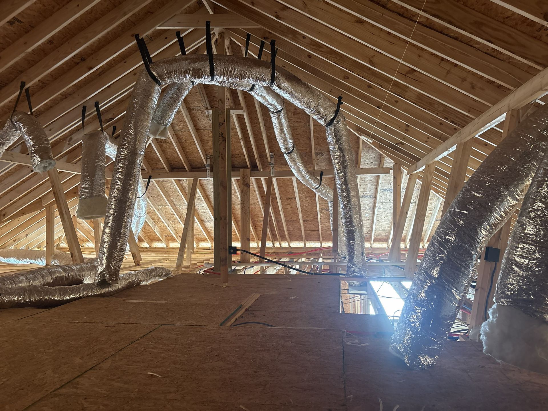 Attic interior showing unfinished wooden rafters and multiple flexible insulated air ducts hanging from the framing.