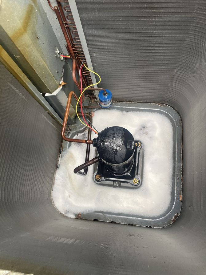 HVAC technician's digital manifold gauge set connected to an outdoor air conditioning unit at night.