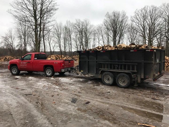 A Red Truck Is Towing a Dumpster Full of Logs — St. Charles, MI — Acorn Tree Service & Landscape Inc