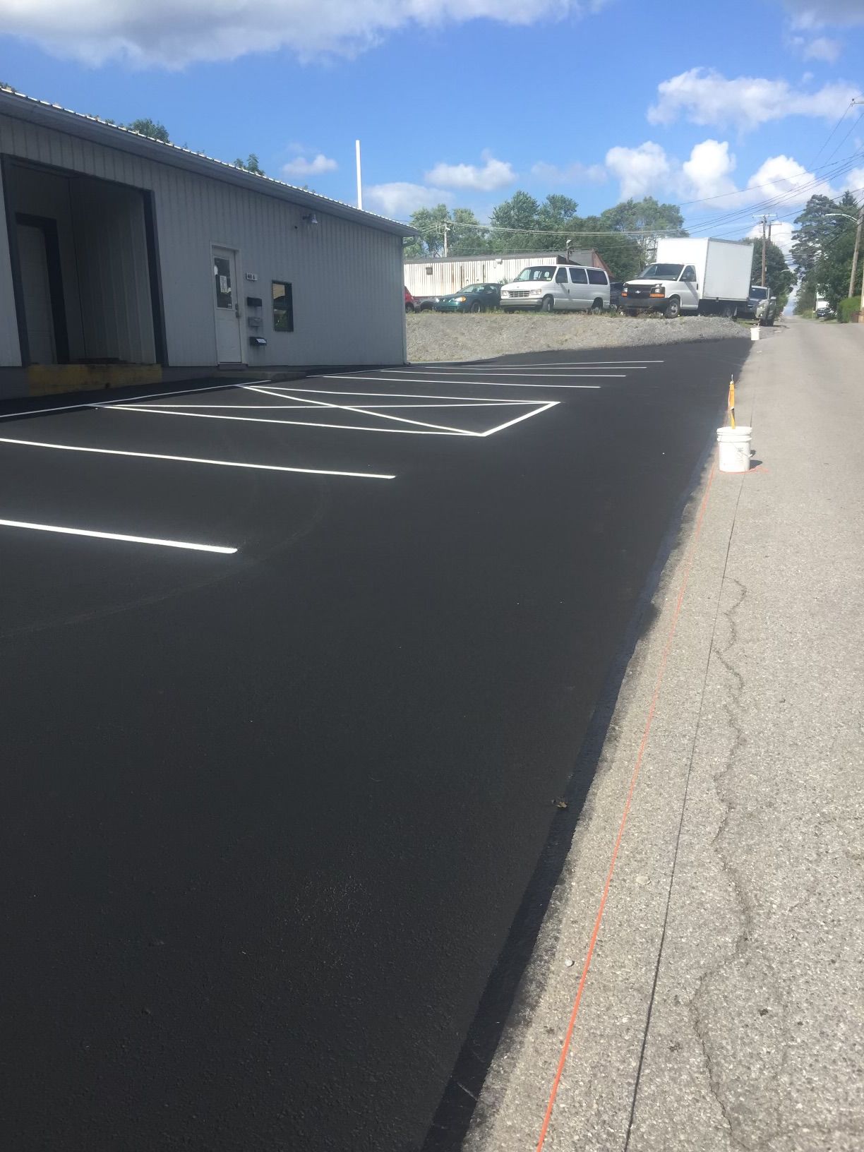 Newly paved asphalt driveway with white parking lines in front of a gray building.