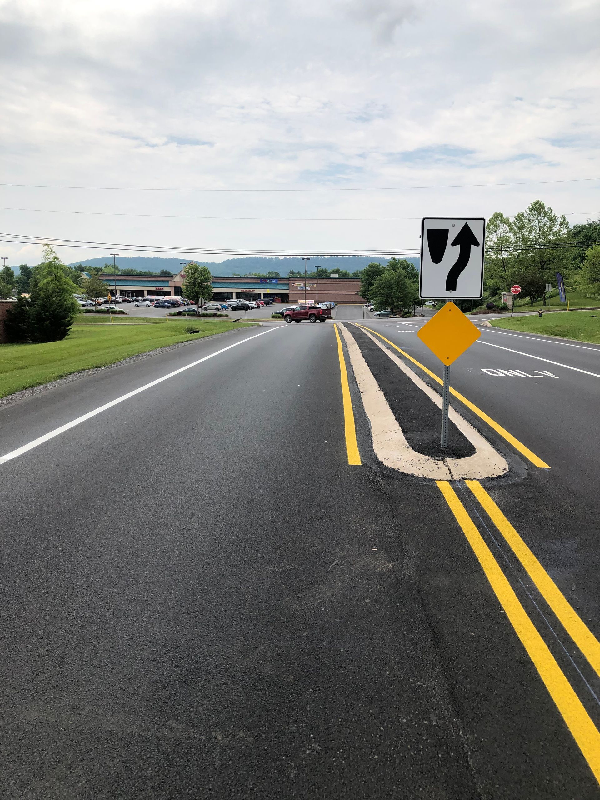 Road with yellow lane markings, a sign indicating a curved route, and a yellow diamond-shaped warning sign.