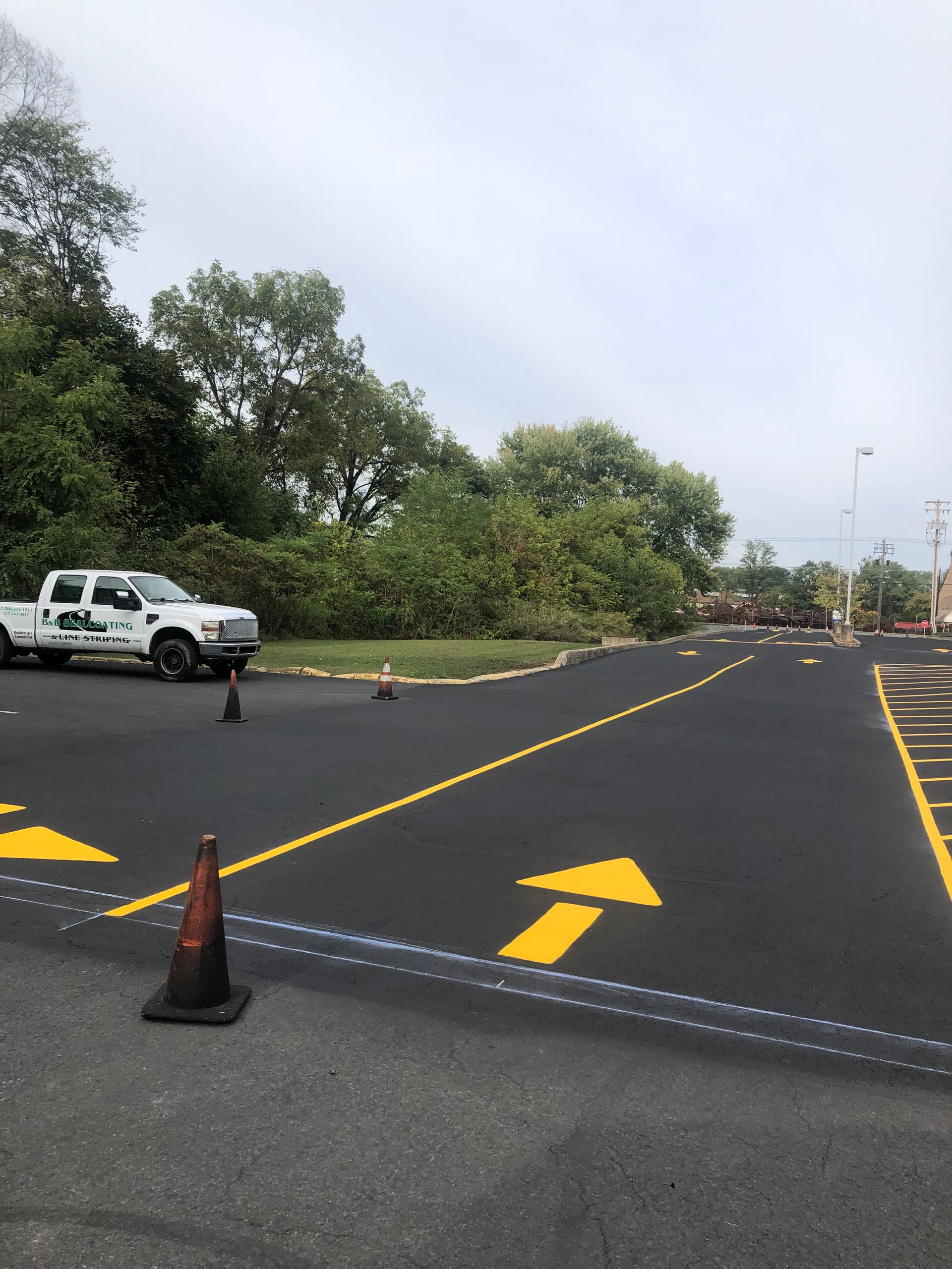 White truck parked on newly paved asphalt with directional arrows and cones. Trees in background.