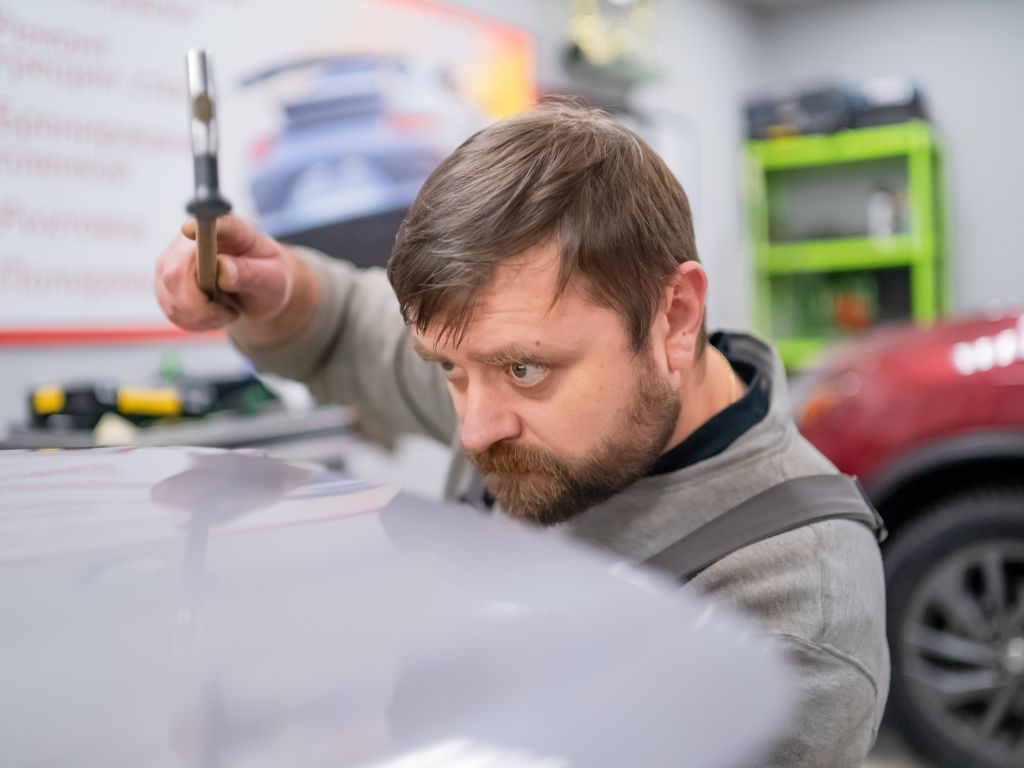 auto body tech working to repair a ding on the hood of a vehicle