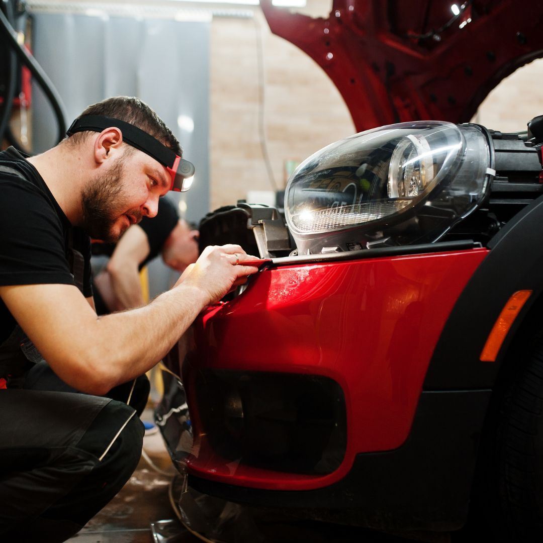 auto technician tucking corners of a freshly applied ppf  for a red car's front fender