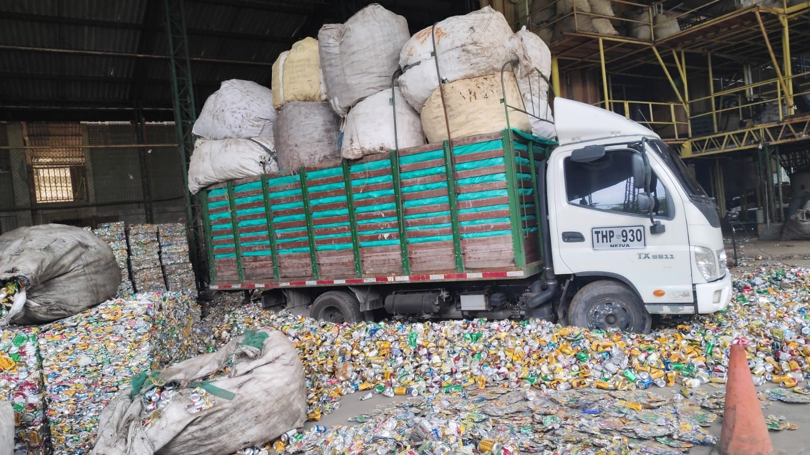 Camión blanco cargado con grandes bolsas de material reciclable en un almacén, rodeado de plástico suelto.