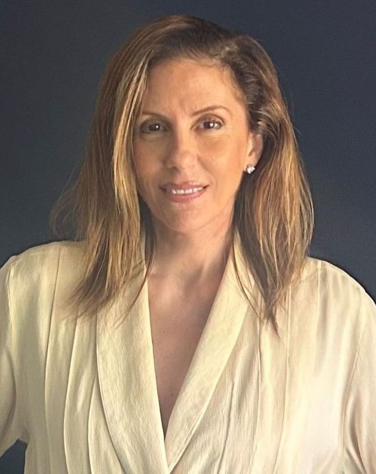 A woman in a white robe is standing in front of a blue wall.