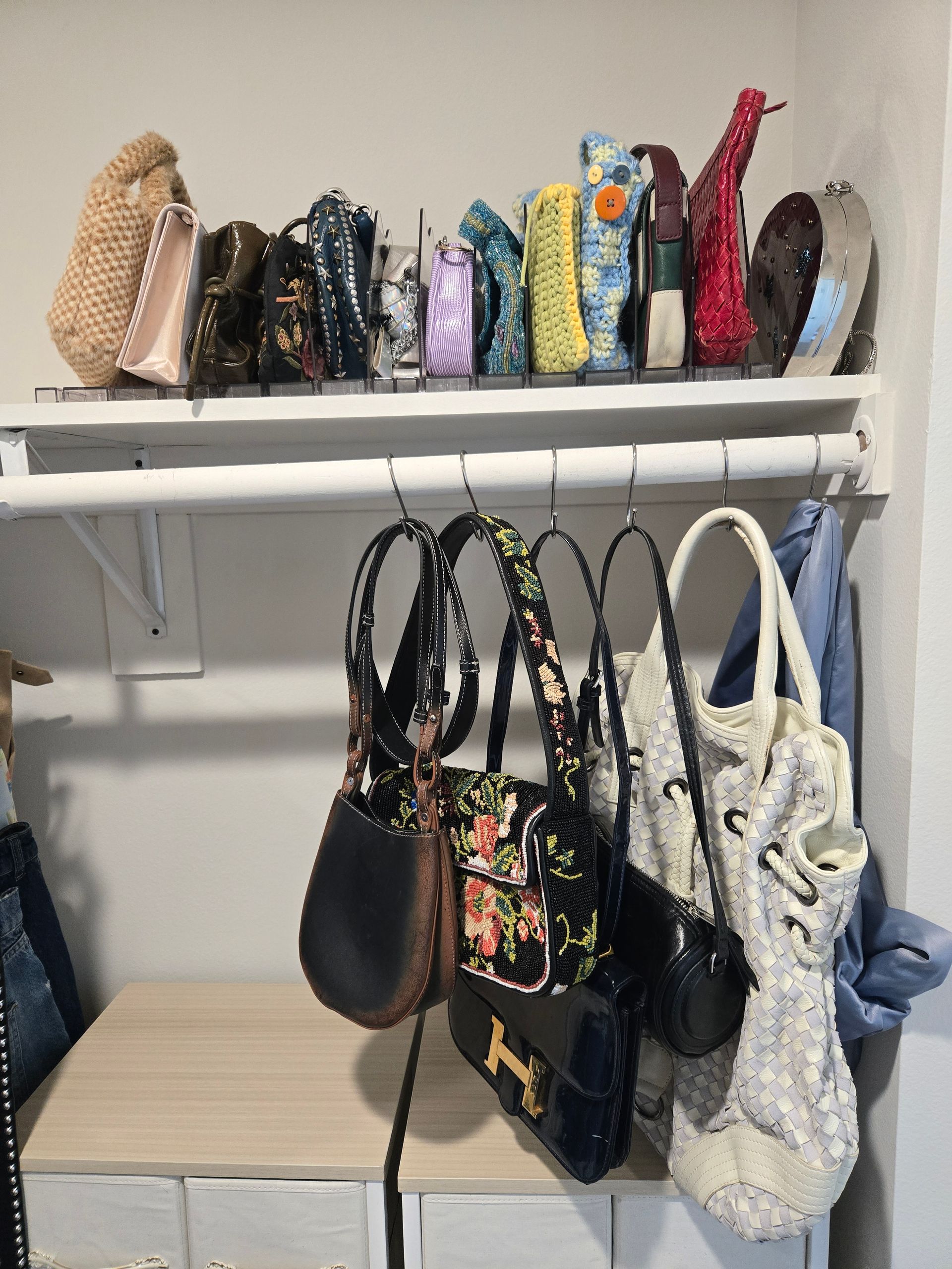 Shelf with handbags and decorative items, plus handbags hanging below.