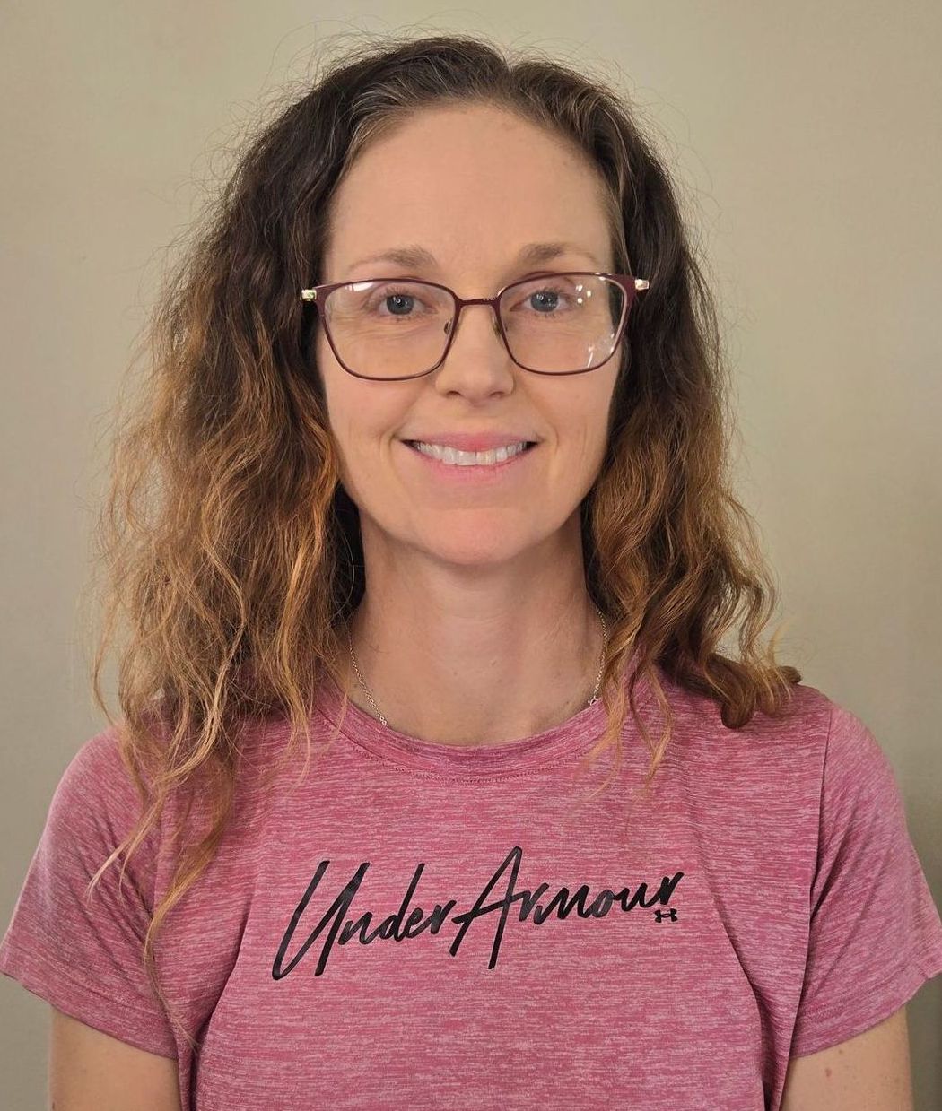 A woman wearing glasses and a pink under armour shirt is smiling.