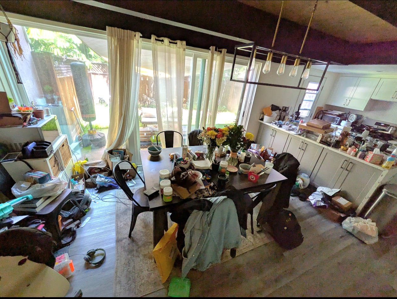 A messy dining room with a table and chairs and a kitchen.