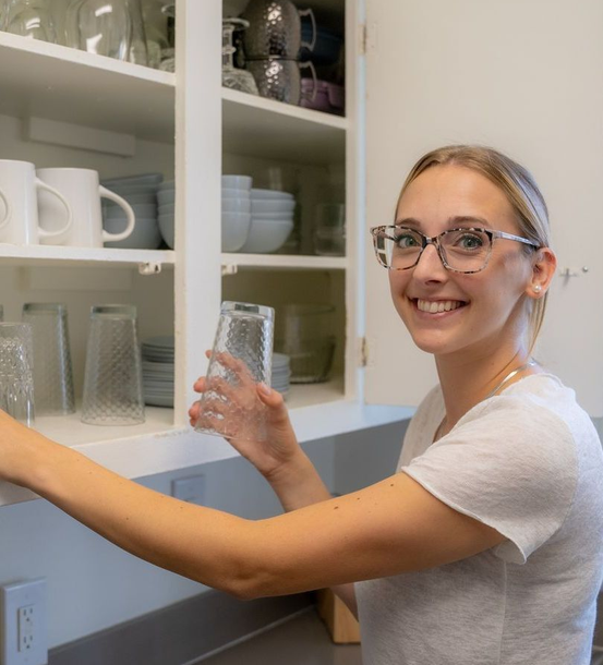 A woman is reaching into a cabinet to take a glass out of it.