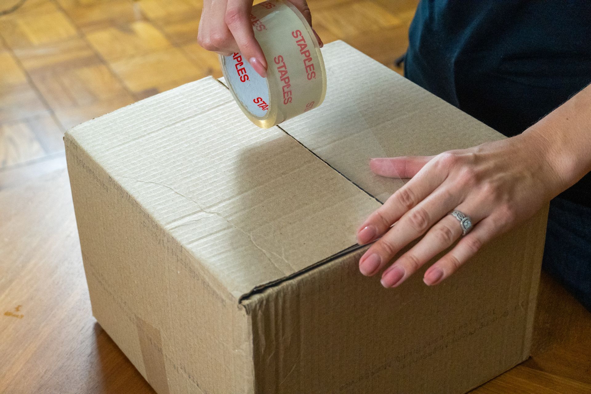 A man is taping a cardboard box with tape.