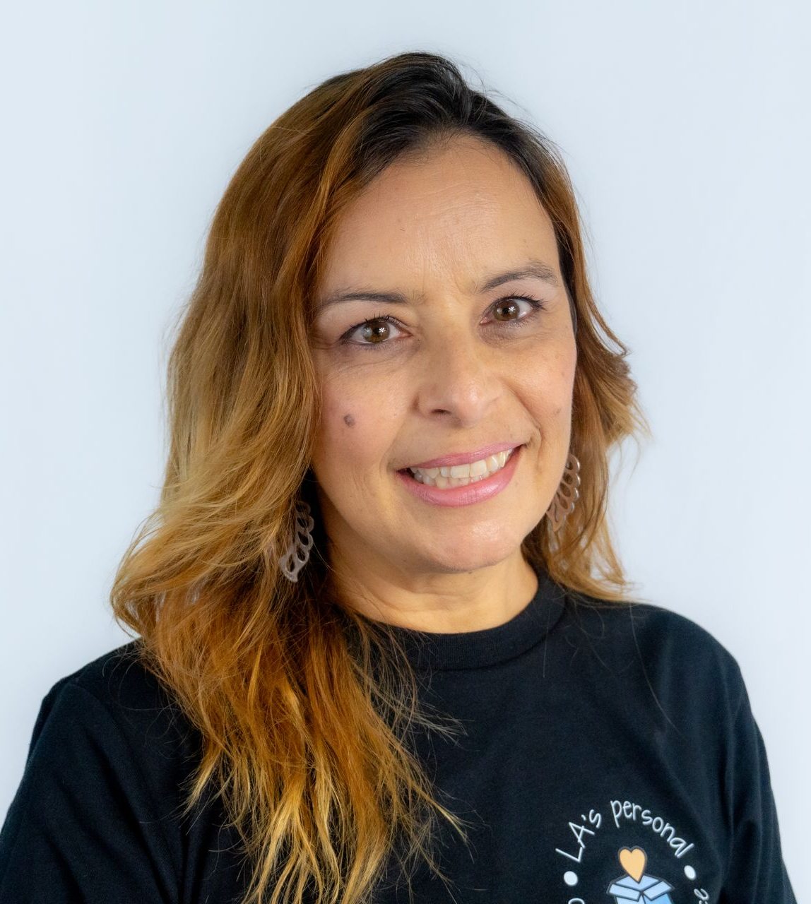 Woman with blonde hair, wearing glasses and a necklace, smiling widely.