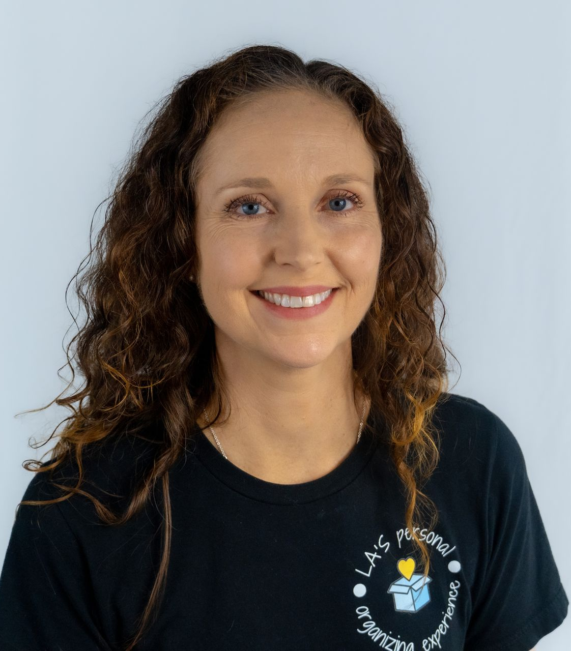 Woman with glasses and curly hair wearing a pink Under Armour shirt smiles at the camera.