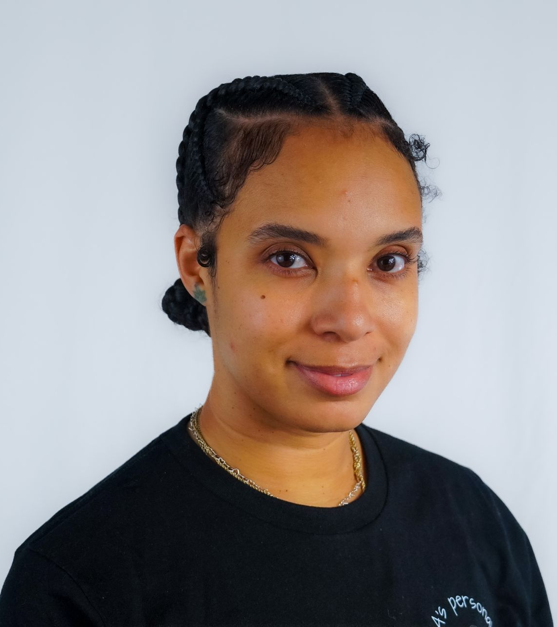 Woman with braids, glasses, and necklaces smiles, wearing a black shirt against a white background.