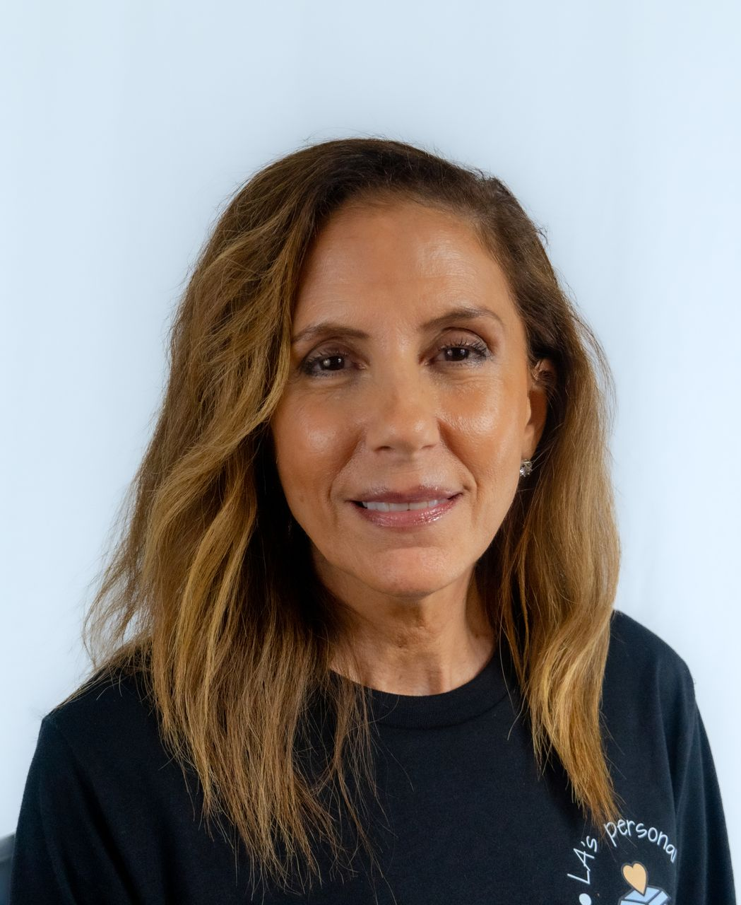 Woman with brown hair smiles, wearing a light-colored shirt against a dark blue background.