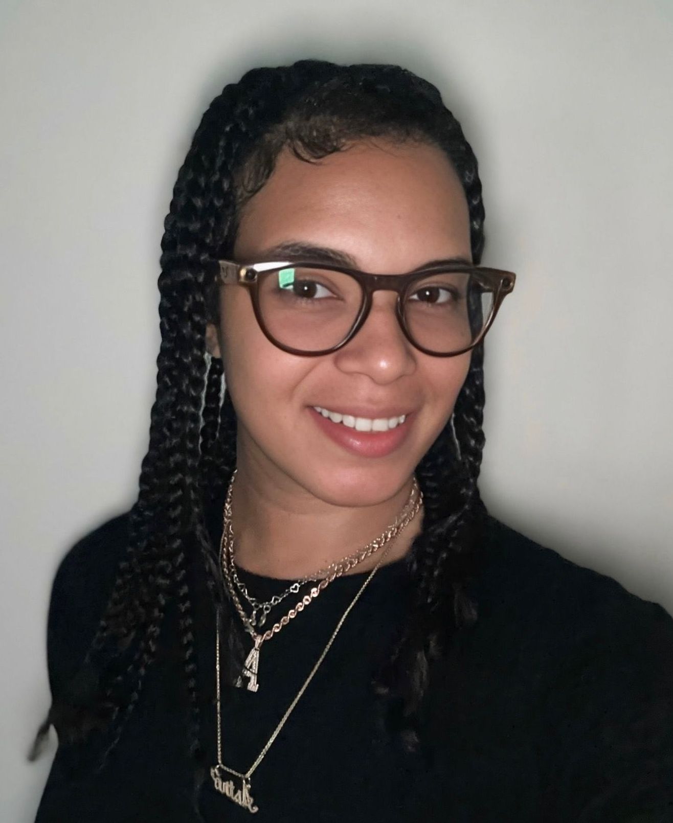 A woman wearing glasses and a necklace is smiling for the camera