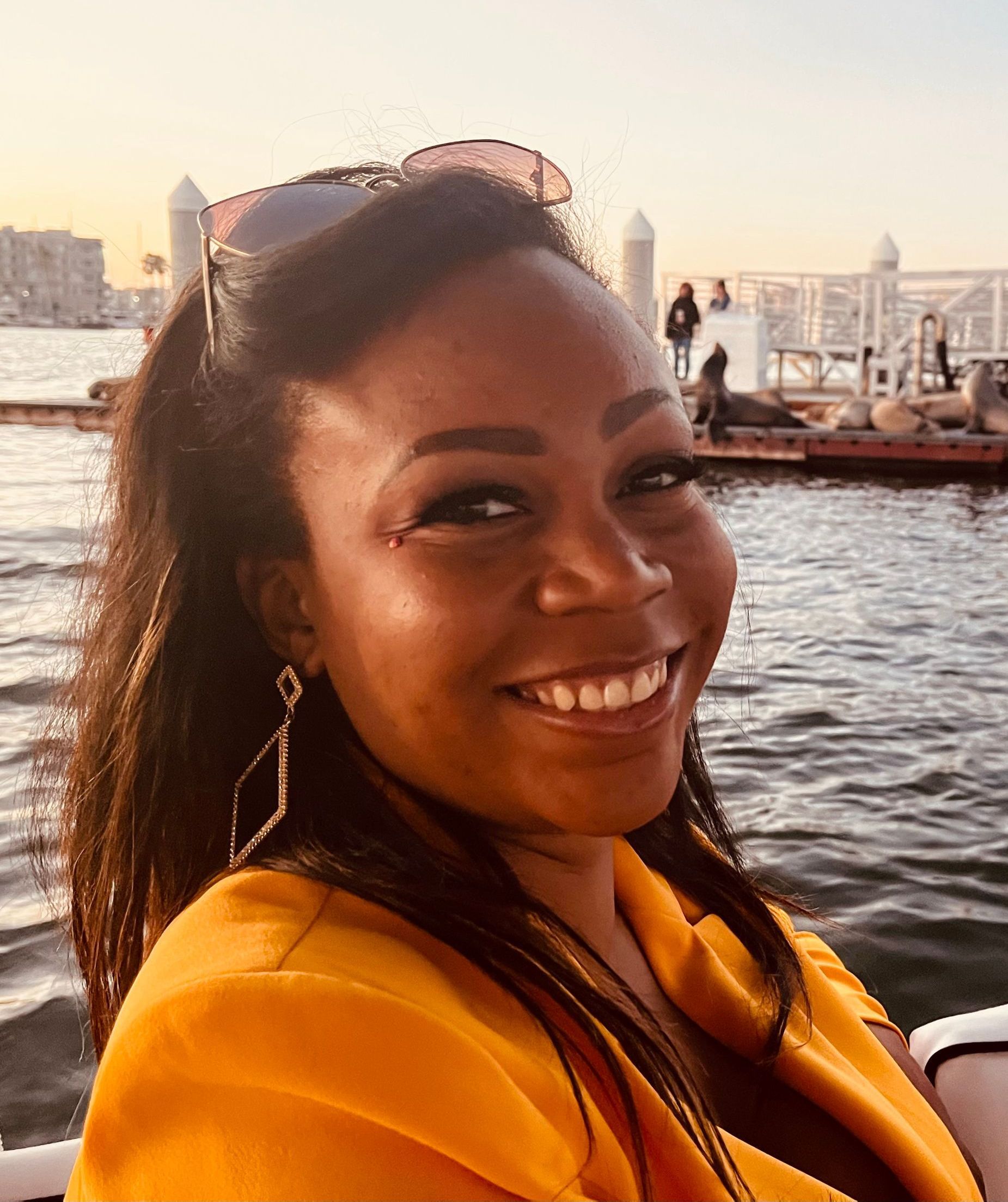A woman in a yellow jacket is smiling in front of a body of water.