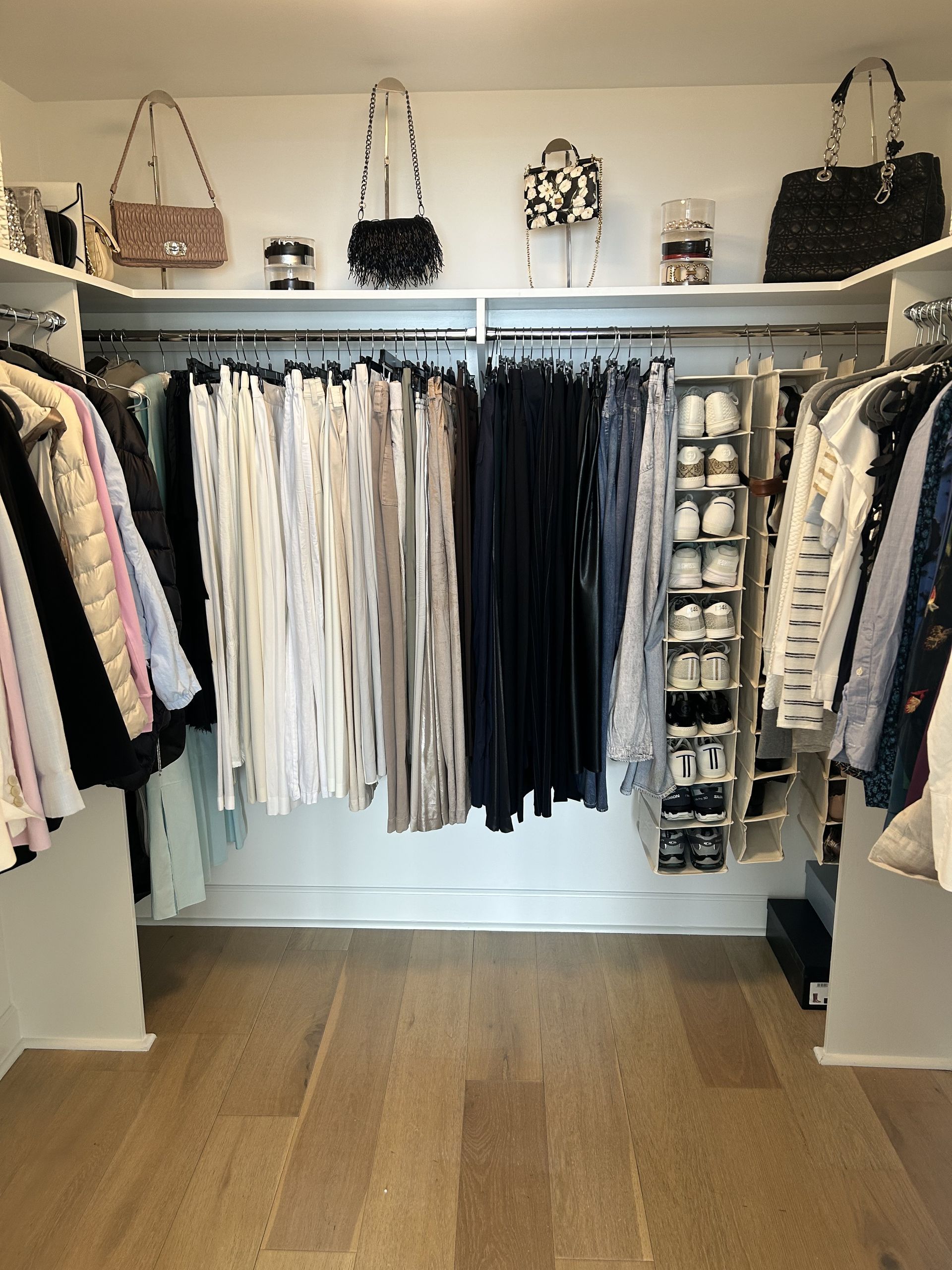 Walk-in closet with organized clothing, shelves with handbags, and hardwood floors.