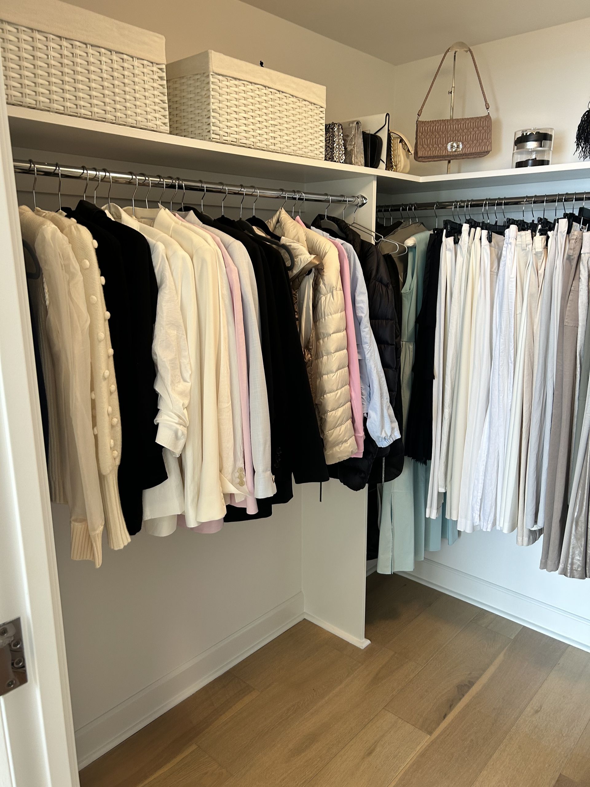 A walk-in closet with hanging clothes, shelves, and light wooden floors.