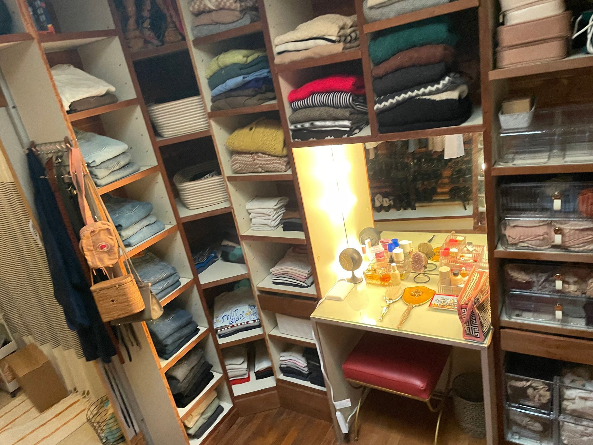 Walk-in closet with angled shelves holding folded clothes. Vanity with mirror and makeup.