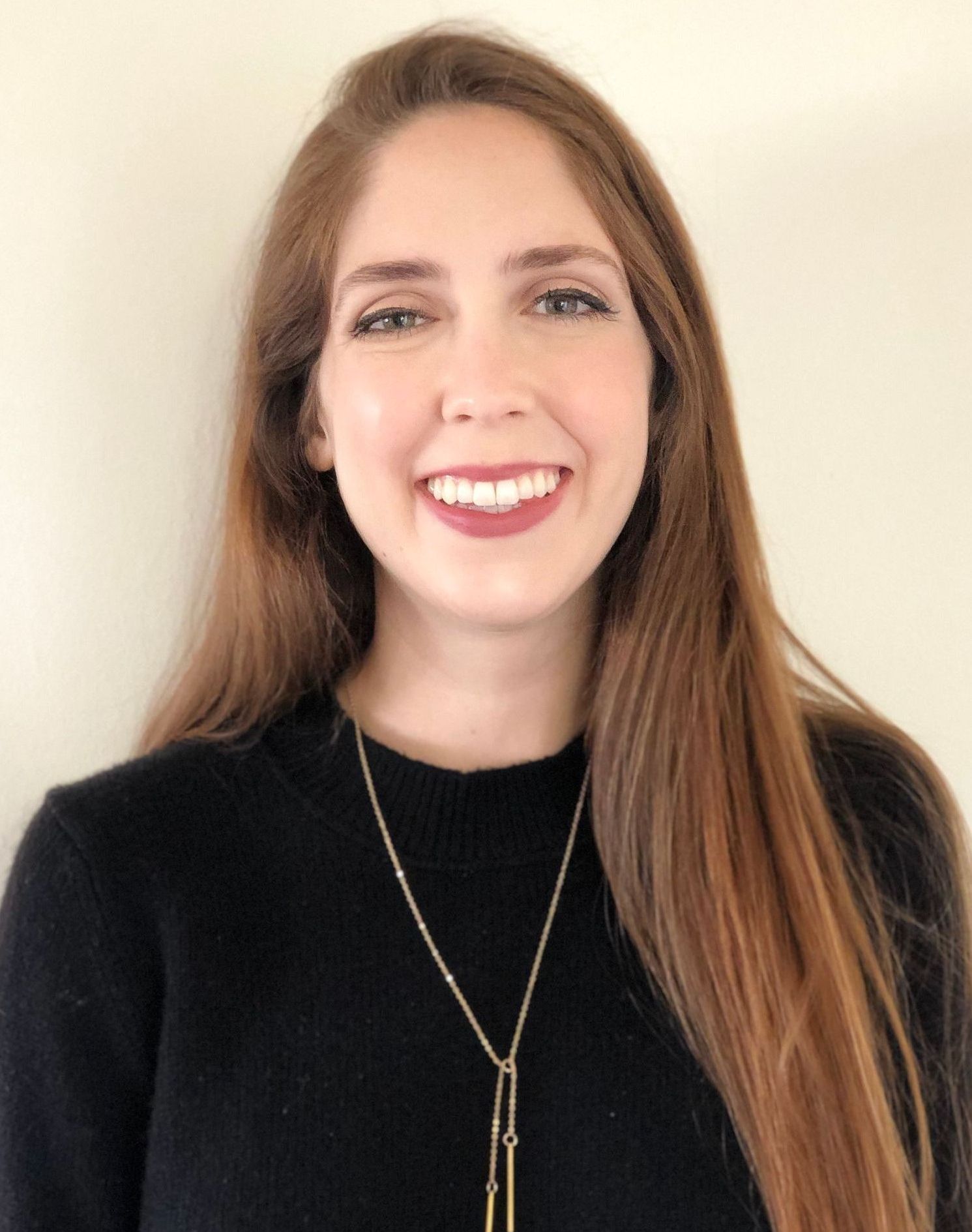 A woman wearing a black sweater and a necklace is smiling for the camera.