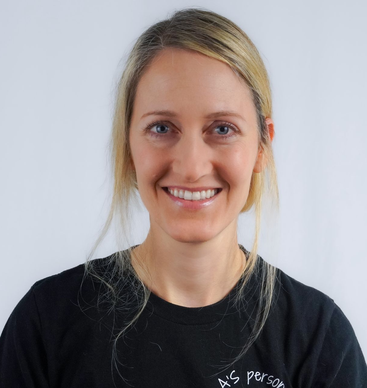 Blonde woman smiling at the camera, wearing a navy polo shirt in front of a brick wall.