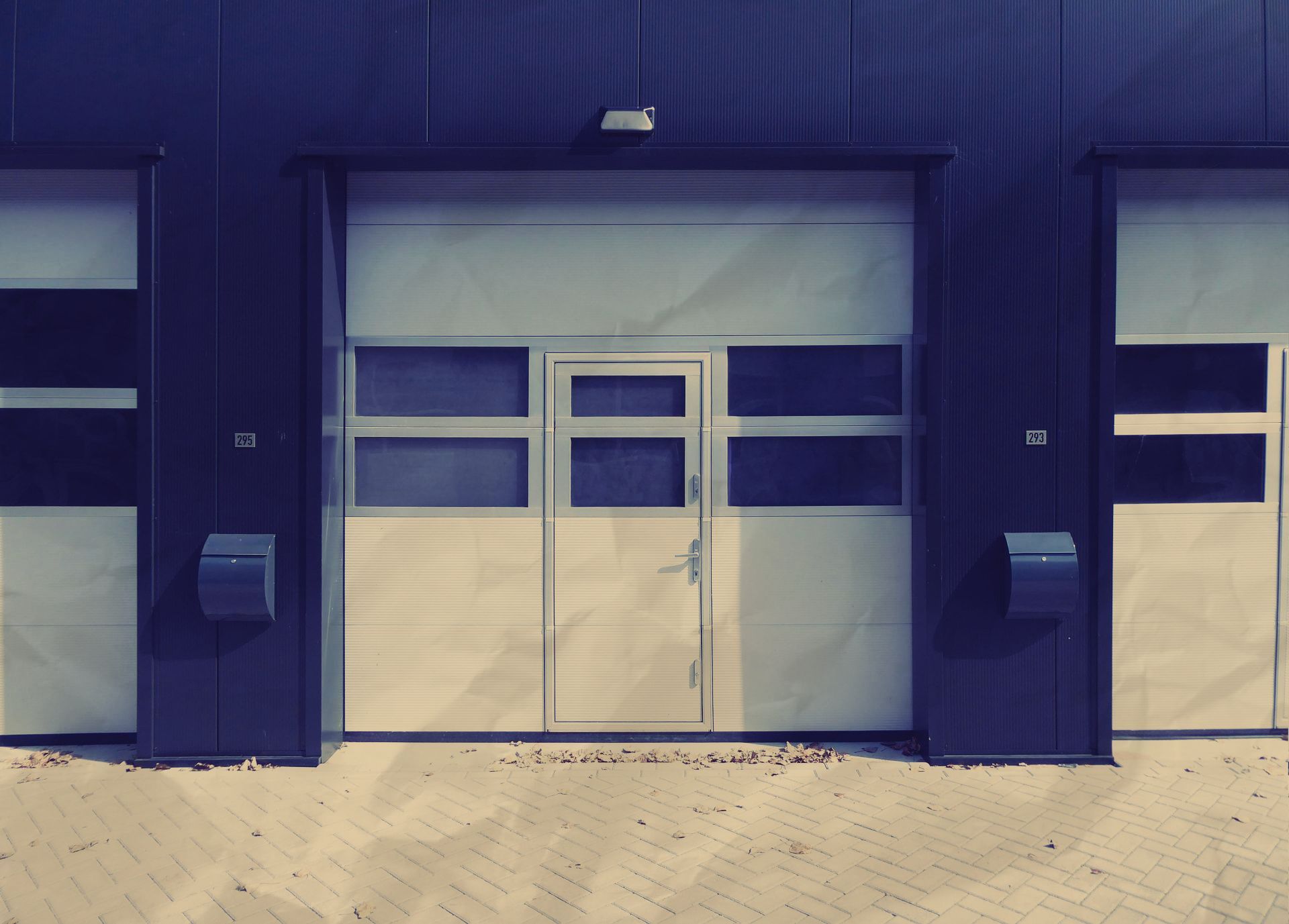 Three white garage doors with a small door in the center, dark blue building, exterior shot.