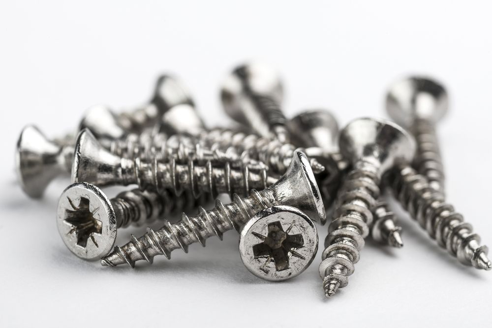 a pile of stainless steel screws on a white surface .