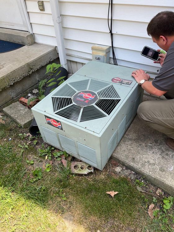 A man is kneeling down next to an air conditioner outside of a house.