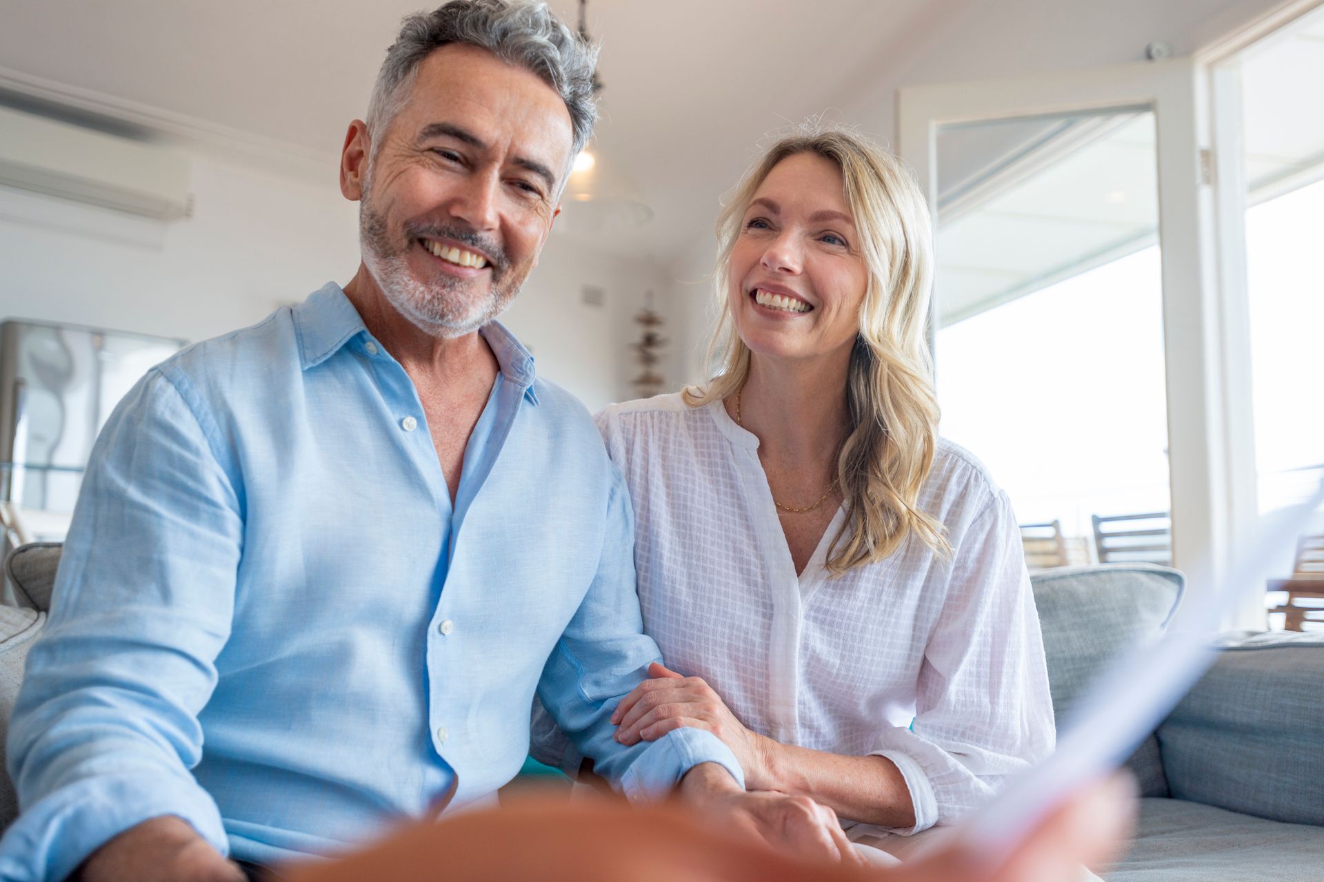 A man and a woman are sitting on a couch looking at a piece of paper.